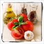 Glasbild Hot & Spicery: Tomaten, Knoblauch, Öl und Gewürzmühlen auf Holz.