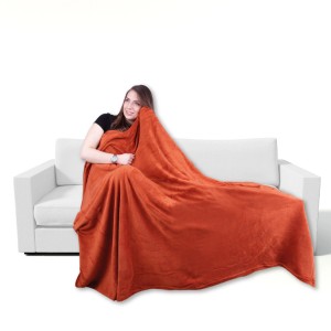 Frau kuschelt in Bestgoodies Mikrofaser Decke Terracotta Ochre auf Sofa. Weiche Wohndecke.