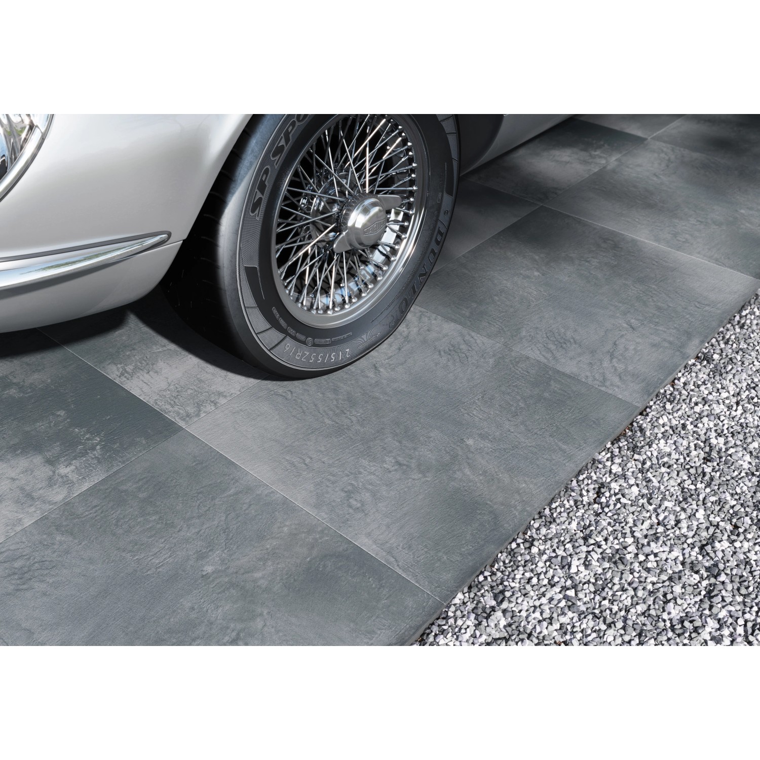 Graue Cersanit Terrassenplatten in Betonoptik, verlegt im Außenbereich neben einem Oldtimer und Kies.