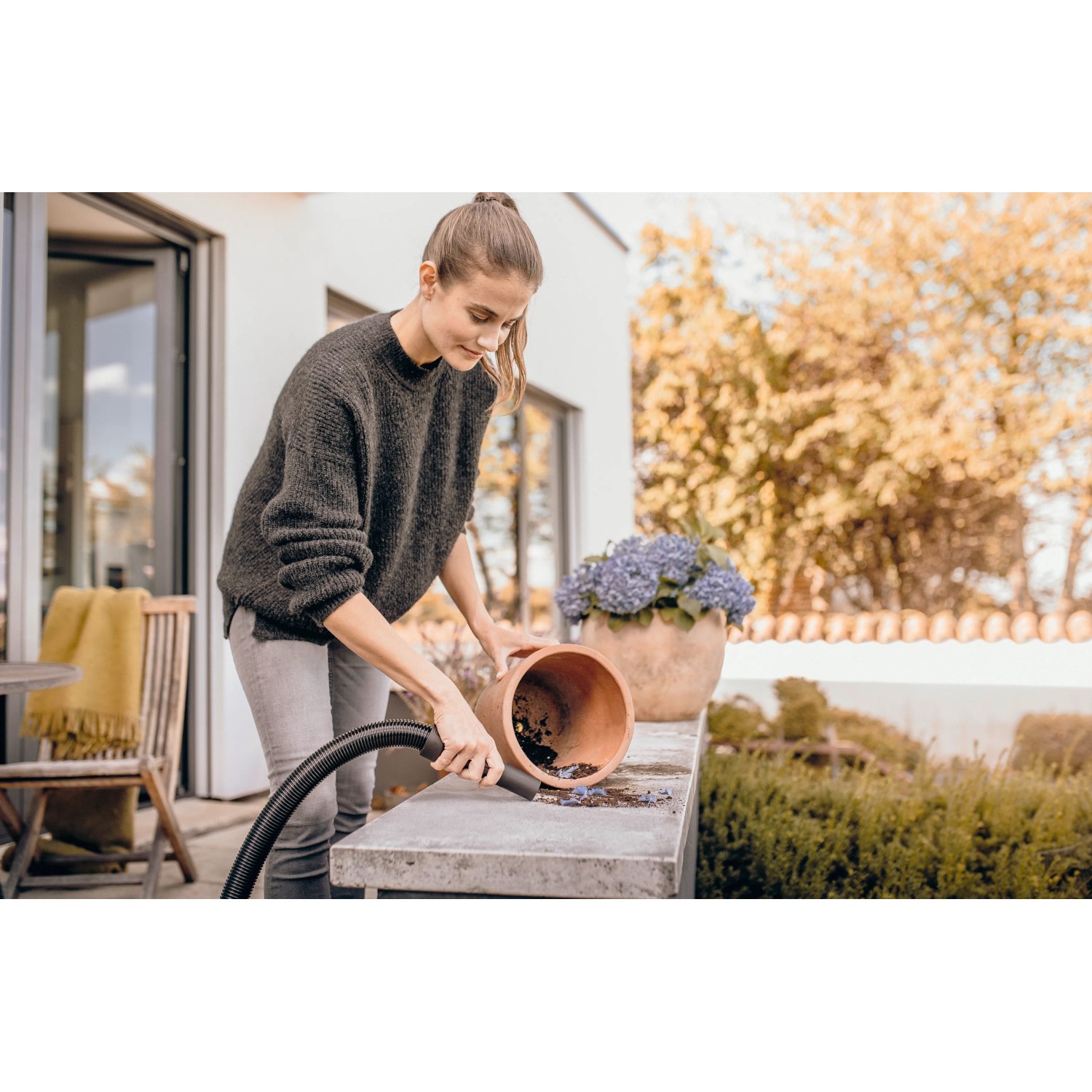 Frau saugt mit Kärcher WD 1 Classic Nass-Trockensauger Erde aus Blumentopf im Garten.