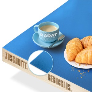 Blaue KARAT Tischfolie Empire (80x235cm) mit abgeschrägter Kante, Kaffeetasse und Croissants auf Tisch.