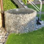 Gabionen-Wasserfass (750 l) im Garten, befüllt mit Steinen. Regentonne mit Gitterabdeckung.