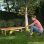 Frau trimmt Rasen unter Bank mit gelbem Kärcher Akku-Rasentrimmer LTR 18-30. Akku-Trimmer für Garten.