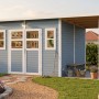 Hellgraues Bertilo Elementgartenhaus Felix 4 Plus XL mit Anbau und Gartenzubehör.
