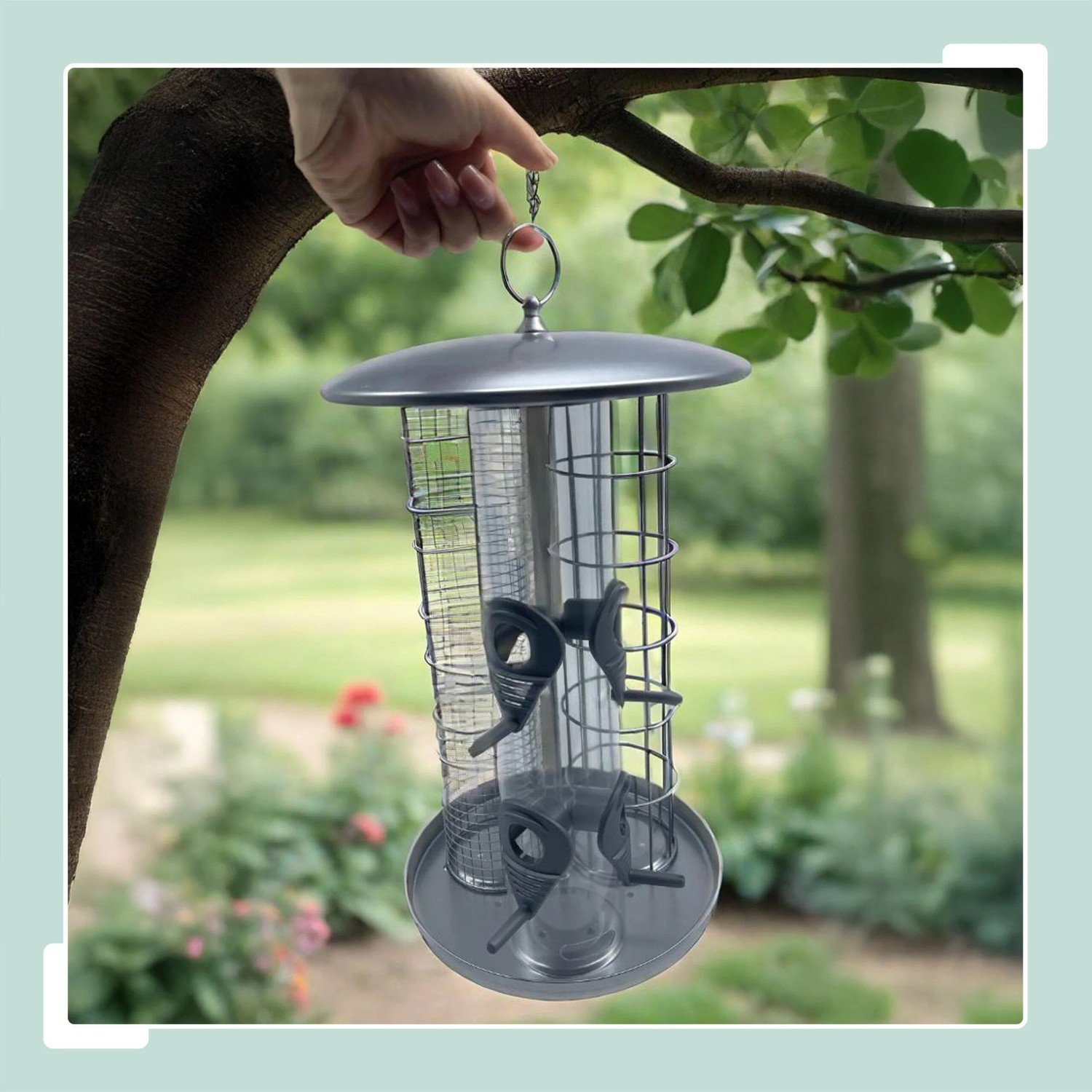 Silberne 3-in-1 Vogelfutterstation aus Eisen und Kunststoff, wetterfest, hängt an Ast im Garten.