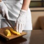 Szene: Person schneidet Mango mit weißen, latexfreien Einmalhandschuhen Gr. L auf Holzbrett.