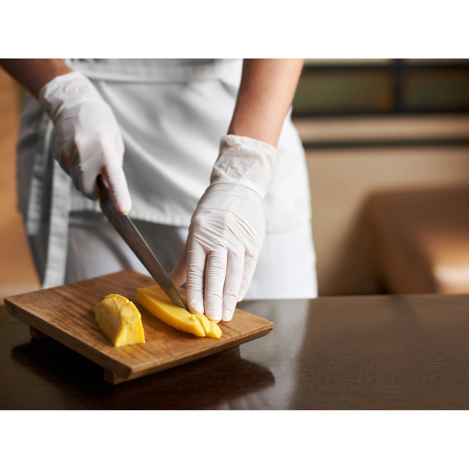 Szene: Person schneidet Mango mit weißen, latexfreien Einmalhandschuhen Gr. L auf Holzbrett.