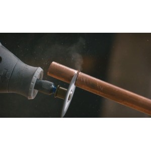 Dremel Miniaturwerkzeug schneidet ein Kupferrohr mit einer Trennscheibe. Staubentwicklung beim präzisen Schnitt.