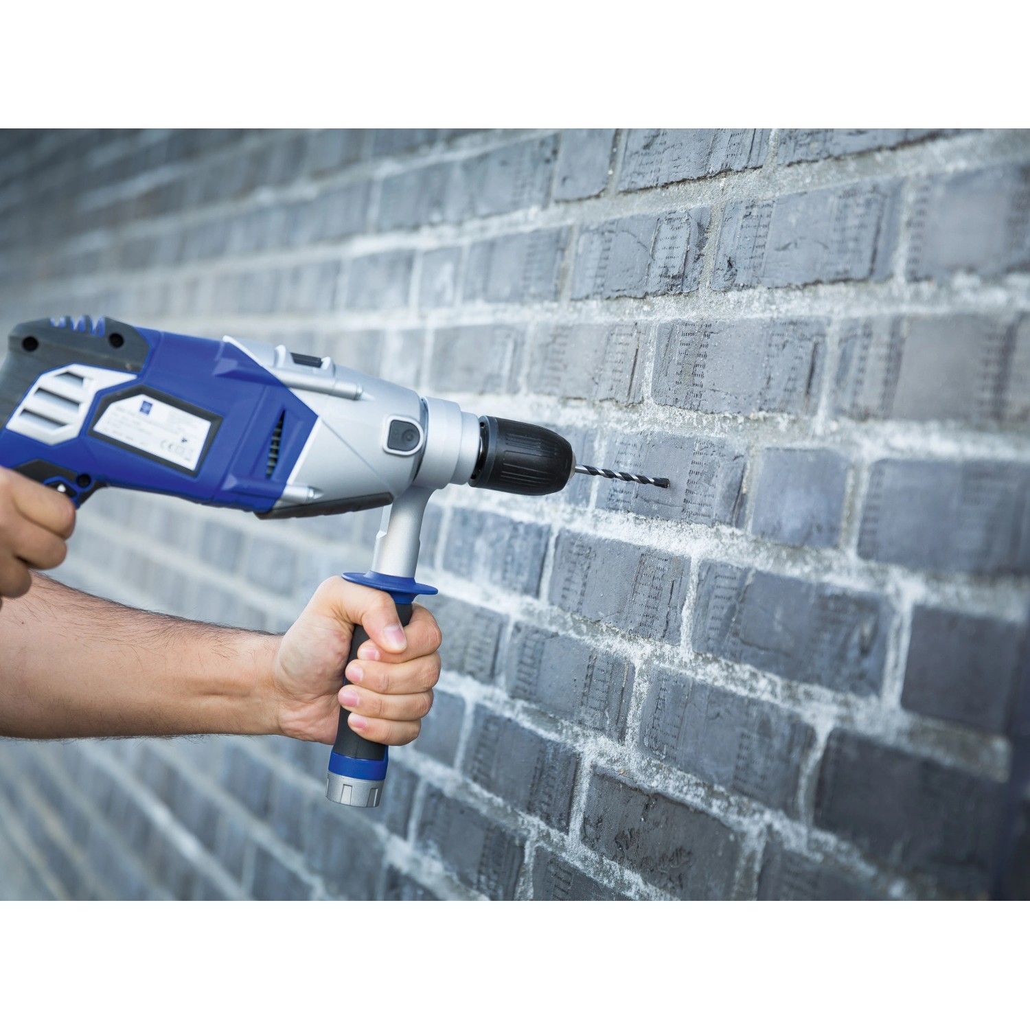 Hand bohrt mit LUX HM Kombibohrer (9mm) Loch in graue Ziegelwand. Universalbohrer im Einsatz.