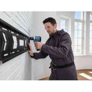 Mann montiert mit Bosch PRO Akku-Bohrschrauber GSR 12V-31 eine Halterung an weißer Wand. Kompakter Bohrschrauber für präzise Arbeiten.