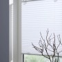Weißes Gardinia Plissee Solo mit Saugnäpfen am Fenster, dekoriert mit Vase und Deko-Häusern.