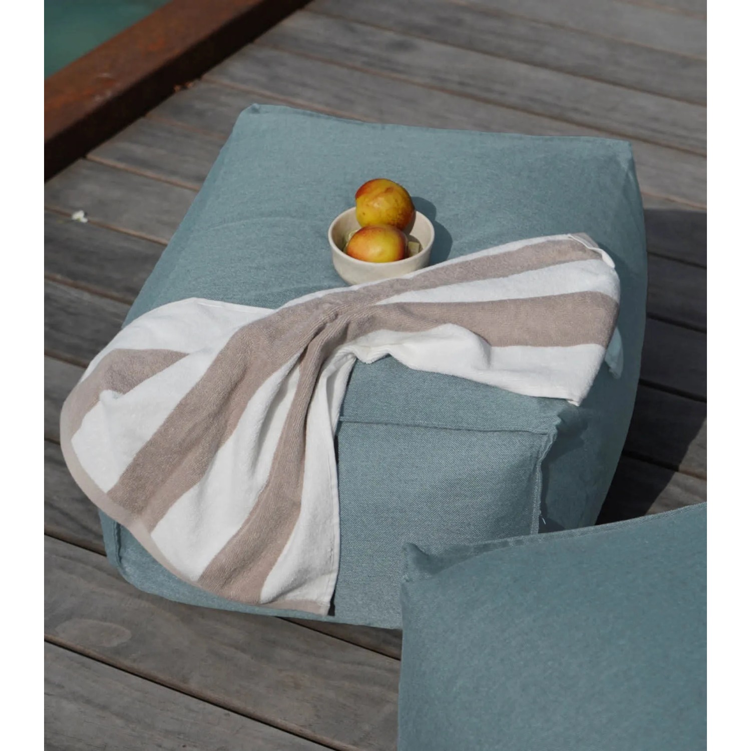 Himmelblauer mokebo Outdoor Pouf mit Handtuch und Obstschale auf Holzterrasse.