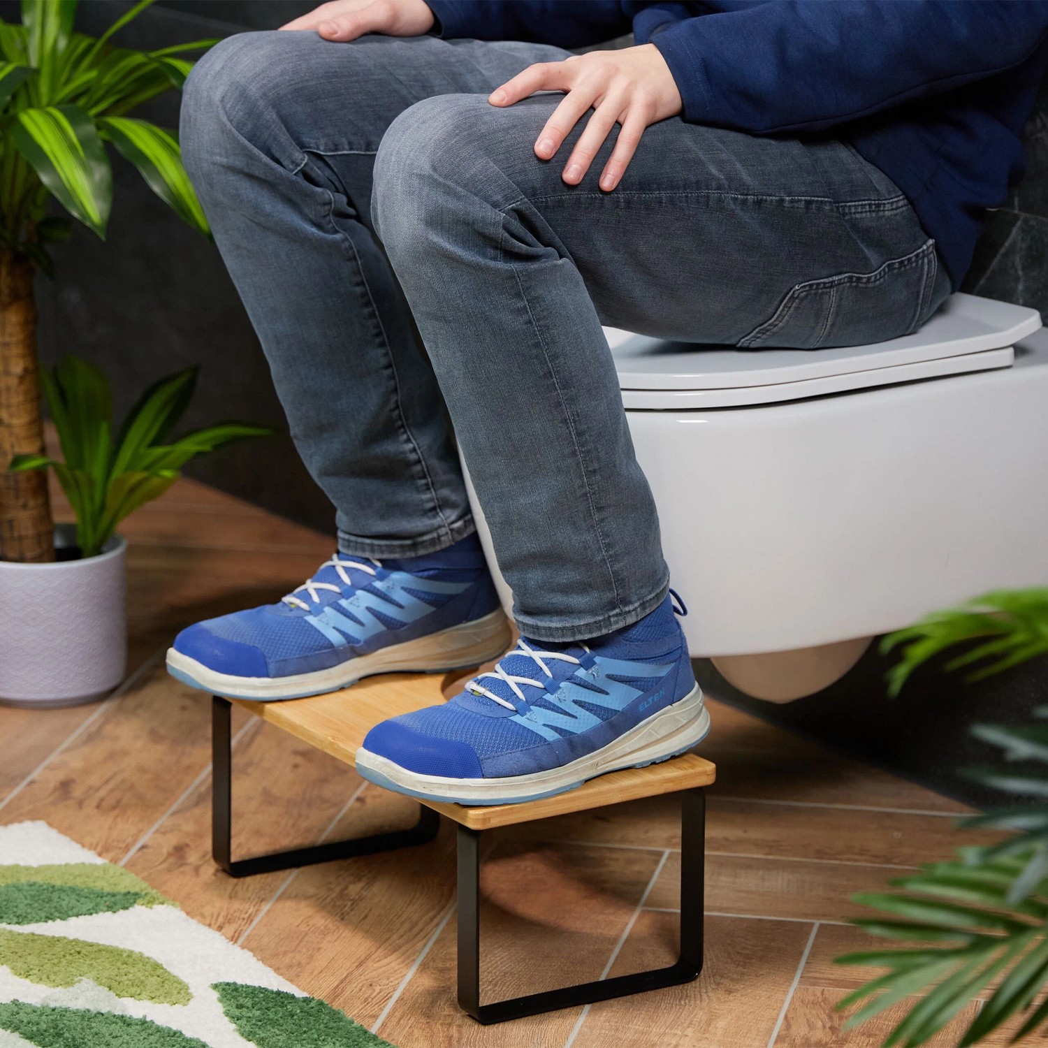 Person nutzt Relaxdays Toilettenhocker aus Bambus mit schwarzen Eisenbeinen für natürliche Hocksitzhaltung. Rutschfester Badhelfer.