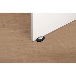 Schwarzer Fix-o-moll Türstopper Dooneo Pebble, selbstklebend, 70x40x26 mm, vor weißer Tür auf Holzboden.