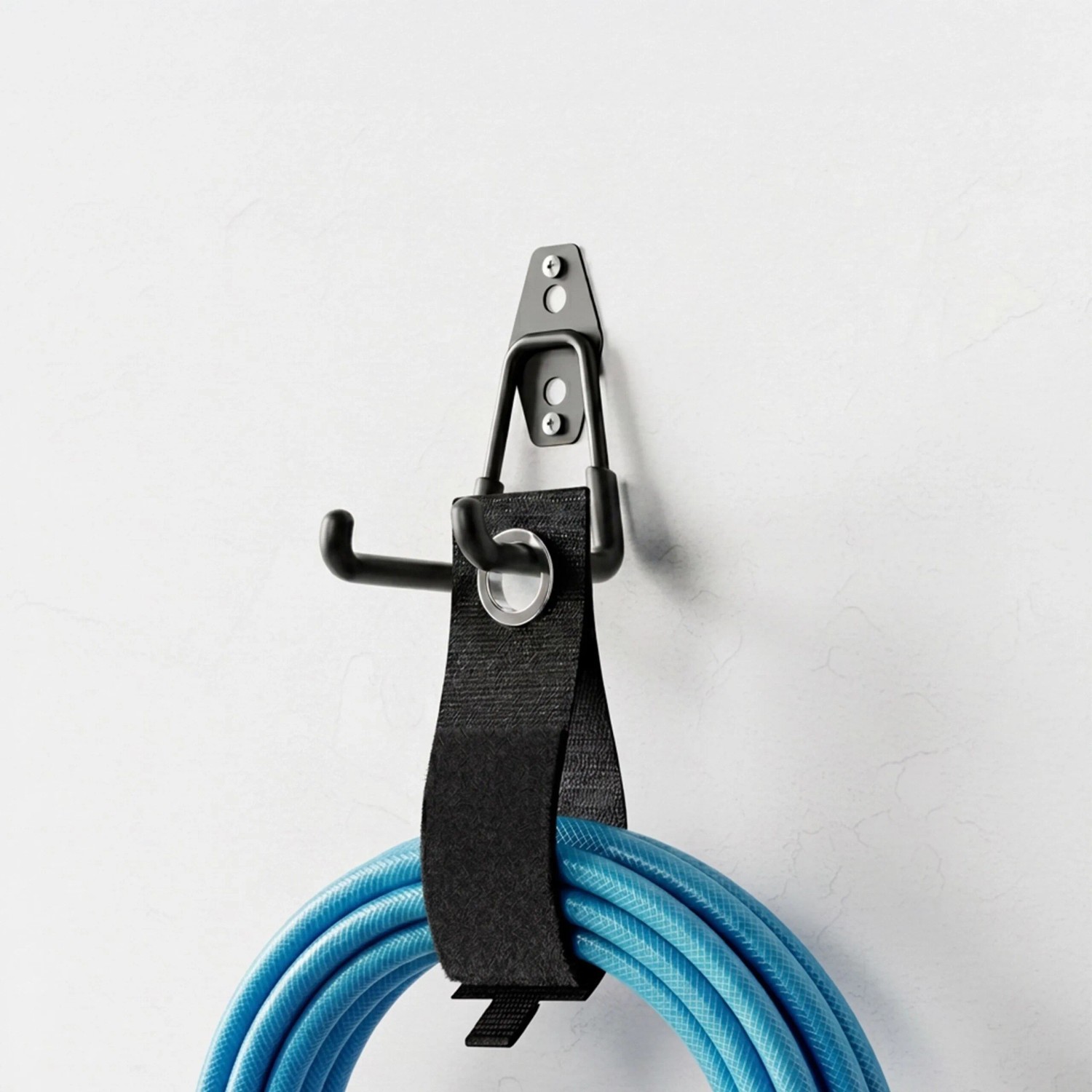 Schwarzer Wandhaken aus Edelstahl mit Organizer-Band hält blauen Schlauch an weißer Wand. Ideal für Garage & Werkstatt.