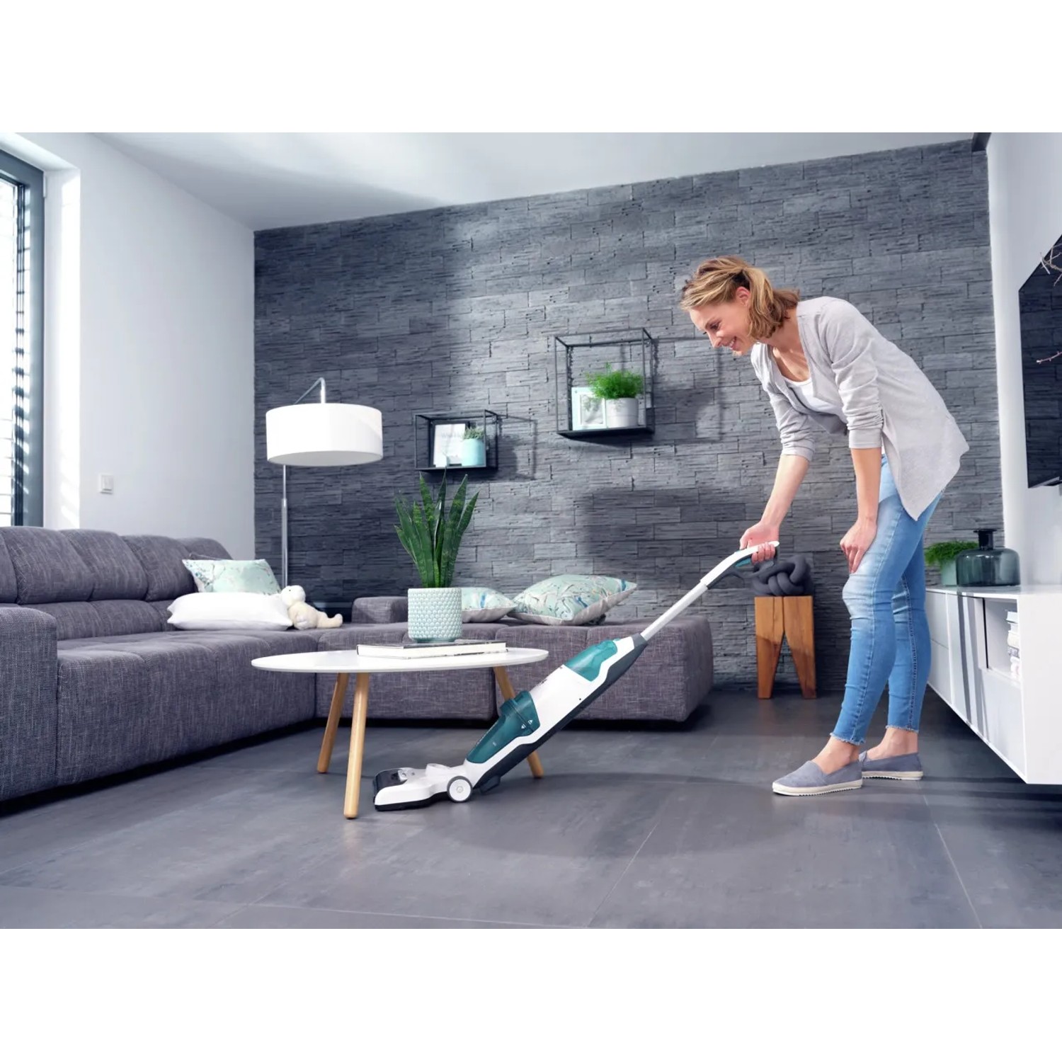 Frau nutzt Leifheit Akku-Saugwischer Regulus Aqua PowerVac zur Bodenreinigung im Wohnzimmer.