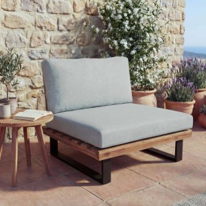 MCW Lounge-Sessel H54 aus hellbraunem Akazienholz mit hellgrauen Polstern auf einer sonnigen Terrasse.