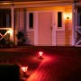Philips Hue Econic LED-Wegeleuchten in Rot beleuchten einen Gartenweg und die Hausfassade.