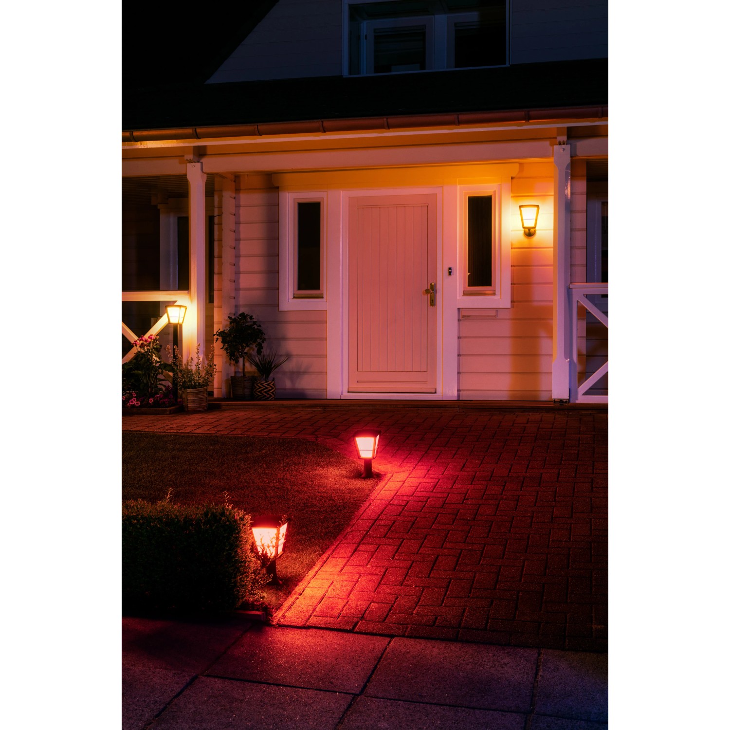 Philips Hue Econic LED-Wegeleuchten in Rot beleuchten einen Gartenweg und die Hausfassade.