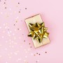 Glänzende goldene Stern-Geschenkschleife auf einem verpackten Geschenk, umgeben von Konfetti. Perfekt für Weihnachtsdekoration.