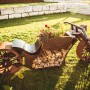 Ferrum Art Design Grillstelle Motorrad in Rostoptik, 123x120cm, mit Holzscheiten und Blumen bepflanzt.