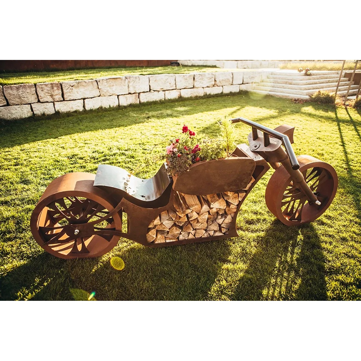 Ferrum Art Design Grillstelle Motorrad in Rostoptik, 123x120cm, mit Holzscheiten und Blumen bepflanzt.