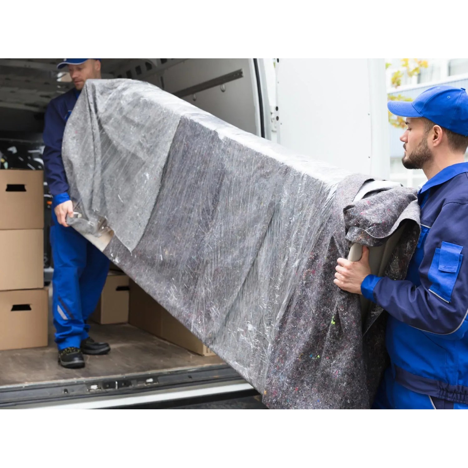 Zwei Umzugshelfer tragen ein mit Primaflor Möbelpackdecken geschütztes Möbelstück aus einem Transporter.