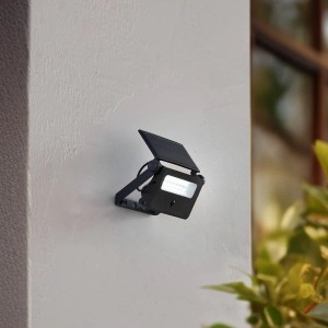 Schwarze Lindby LED Solar Wandleuchte Rikad mit Bewegungsmelder an heller Wand.