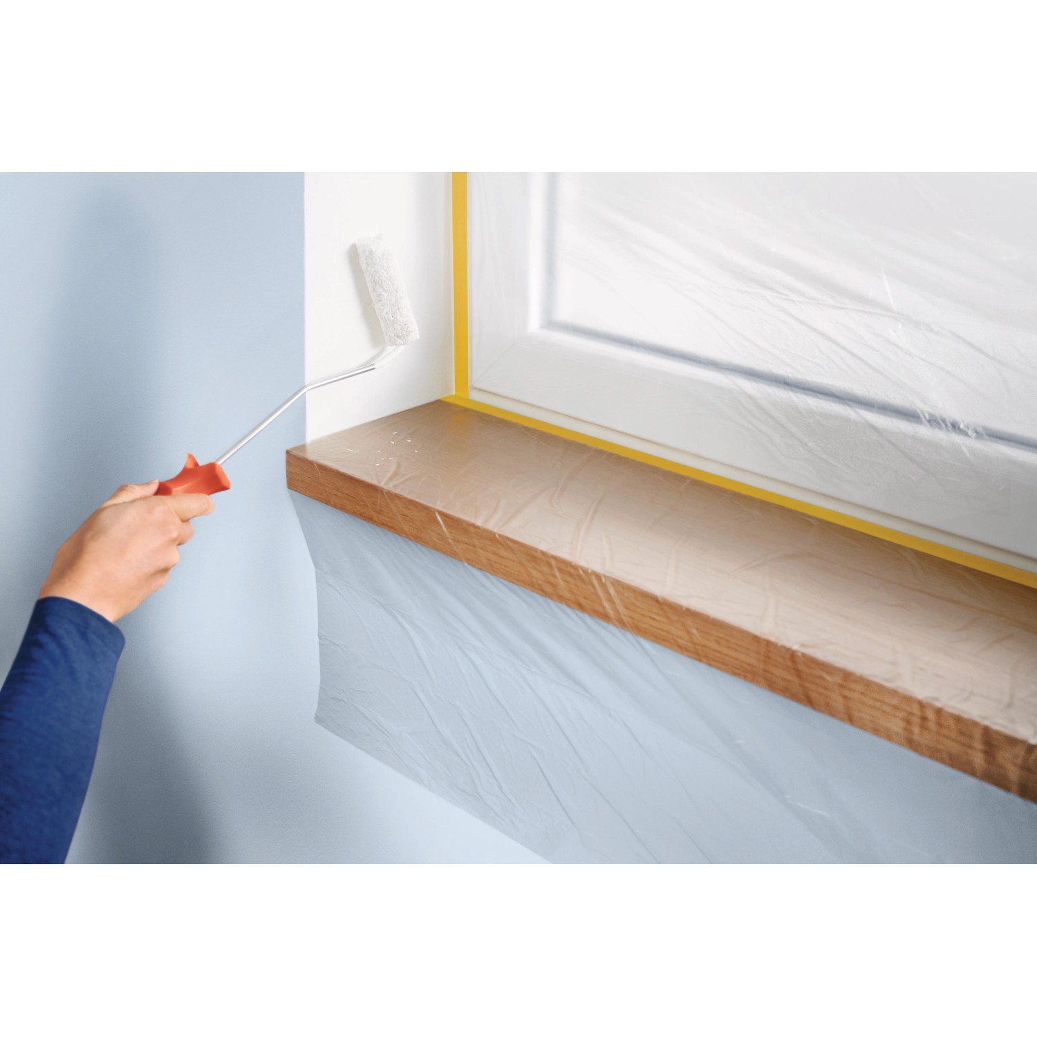 Anwendung der Tesa Abdeckfolie Easy Cover: Fensterbank und Fensterrahmen sind mit Folie und Klebeband geschützt.