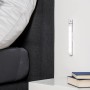 Weiße Müller-Licht LED Unterbauleuchte Falis mit Sensor an einer Wand über einem Nachttisch.