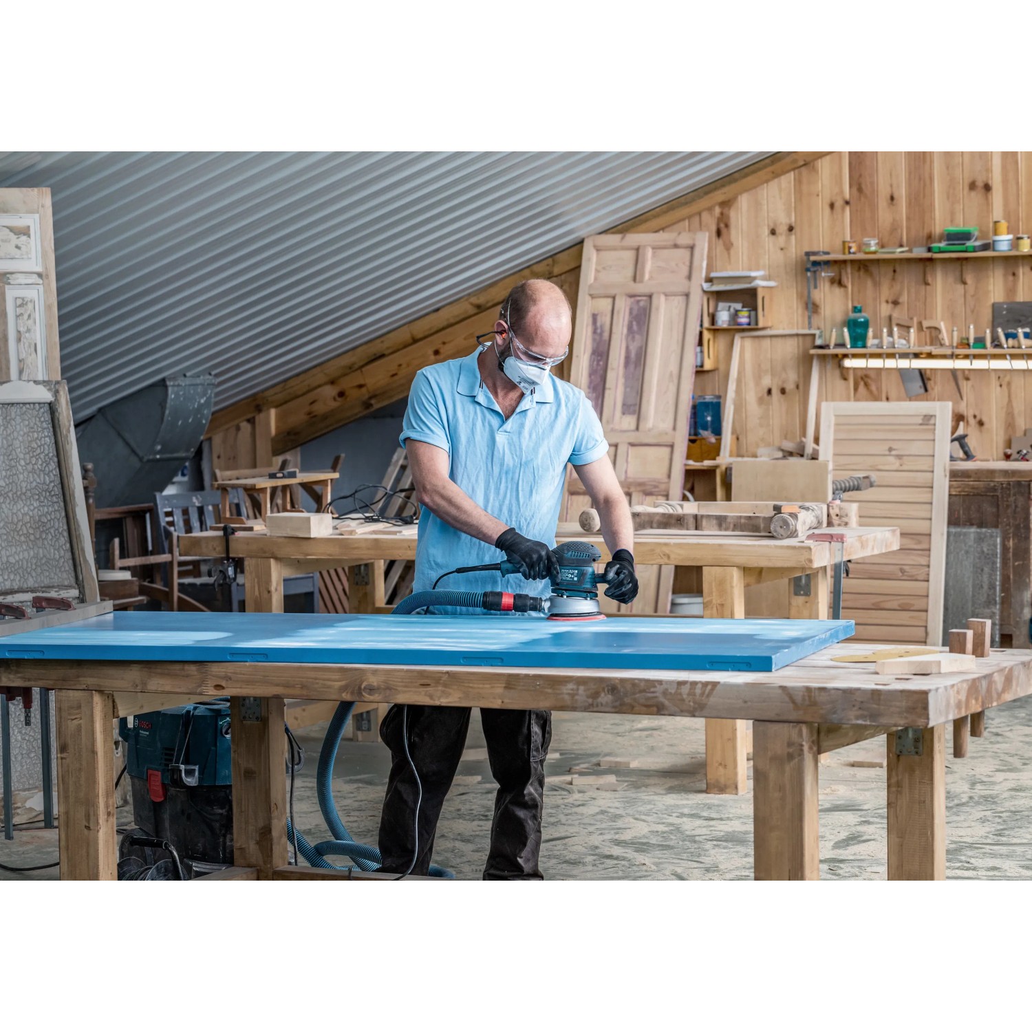 Handwerker schleift blaue Holzplatte mit Bosch Exzenterschleifer und Schleifblatt C470.