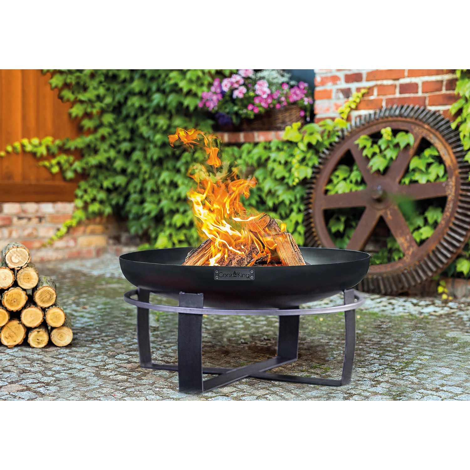 Schwarze Wilk Feuerschale Viking Ø 60 cm mit brennendem Holz auf einem Gartensitzplatz.