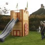 Axi Arthur Spielhaus aus Holz mit grauer Rutsche und zwei Kindern beim Spielen im Garten.