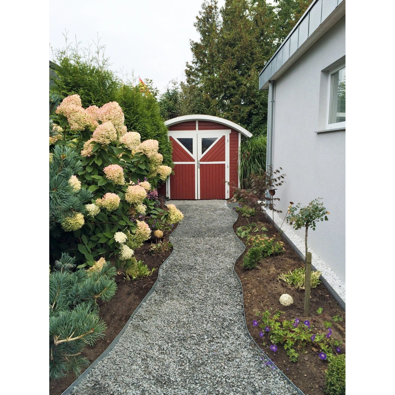 Gartenweg mit ACO Self® Kieswabe eco S befestigt, führt zu rotem Gartenhaus.