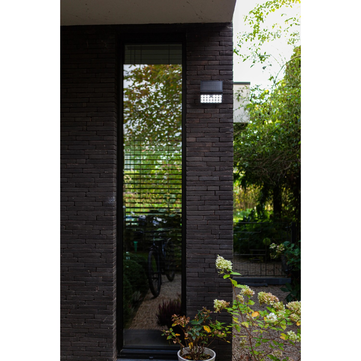 Schwarze Lutec LED Solar-Wandleuchte Tuda mit Bewegungsmelder außen an einer Hauswand.