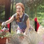 Frau gießt Blumen mit Relaxdays Kniebank im Garten. Klappbarer Gartenhocker mit Taschen.