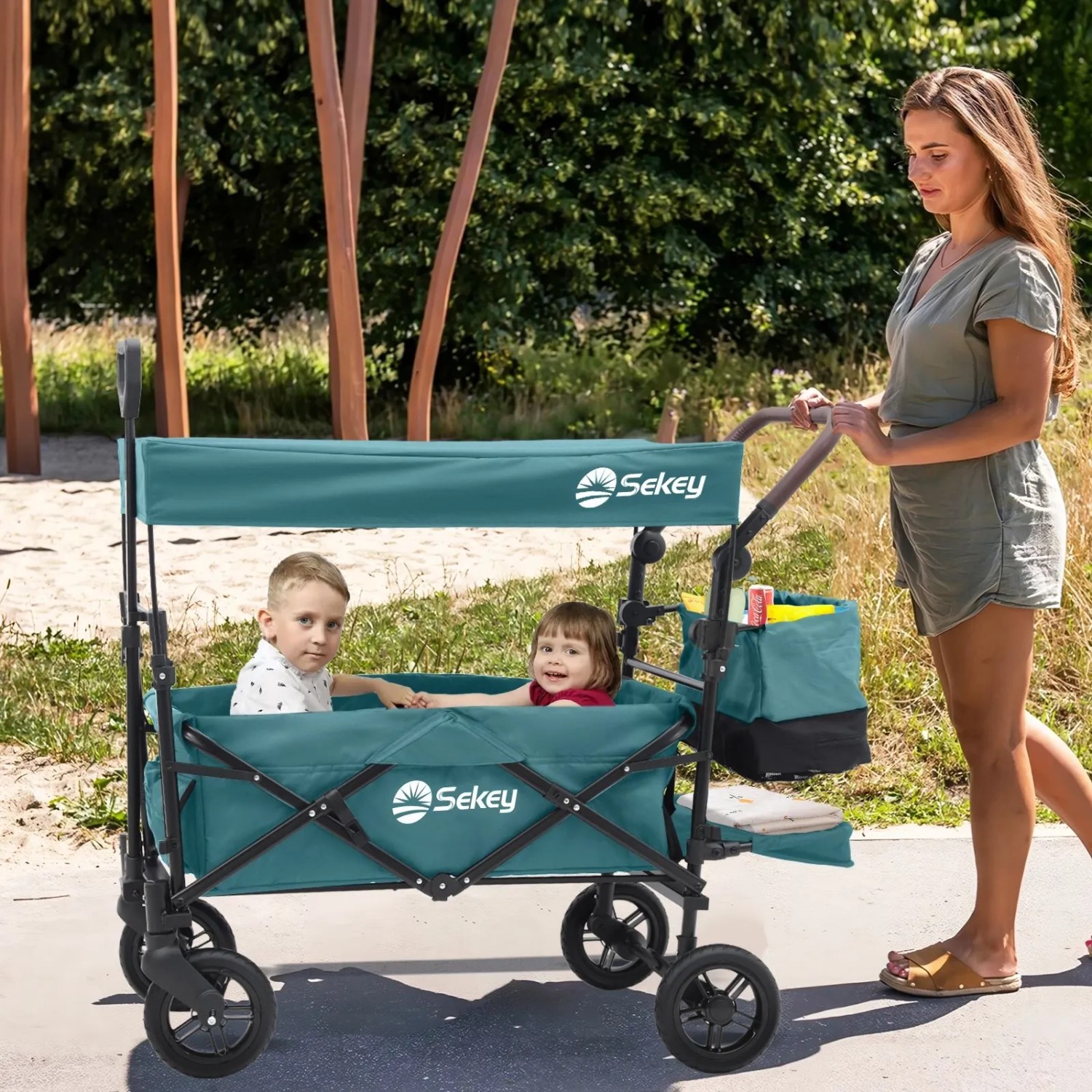 Sekey Bollerwagen mit Dach, blaugrün, mit zwei Kindern und einer Frau im Park.