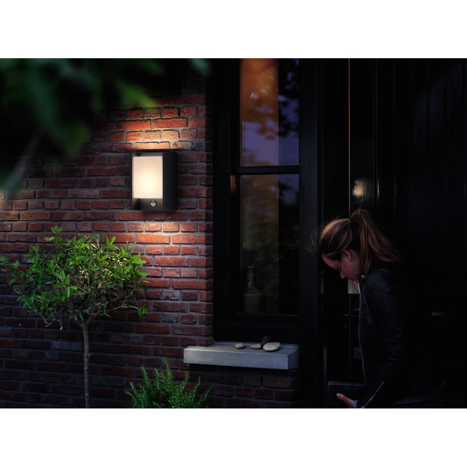 Anthrazitfarbene LED-Außenwandleuchte Arbour mit Sensor an einer Backsteinwand.
