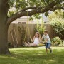 Gelbe Relaxdays Nestschaukel im Garten. Zwei lachende Kinder schaukeln auf der runden Kinderschaukel an einem Baum.
