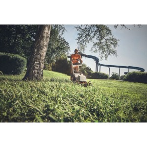 Mann mäht hohes Gras mit orange-grauem Stihl Akku-Rasenmäher RMA 756 V im Park. Professionelle Gartenpflege.