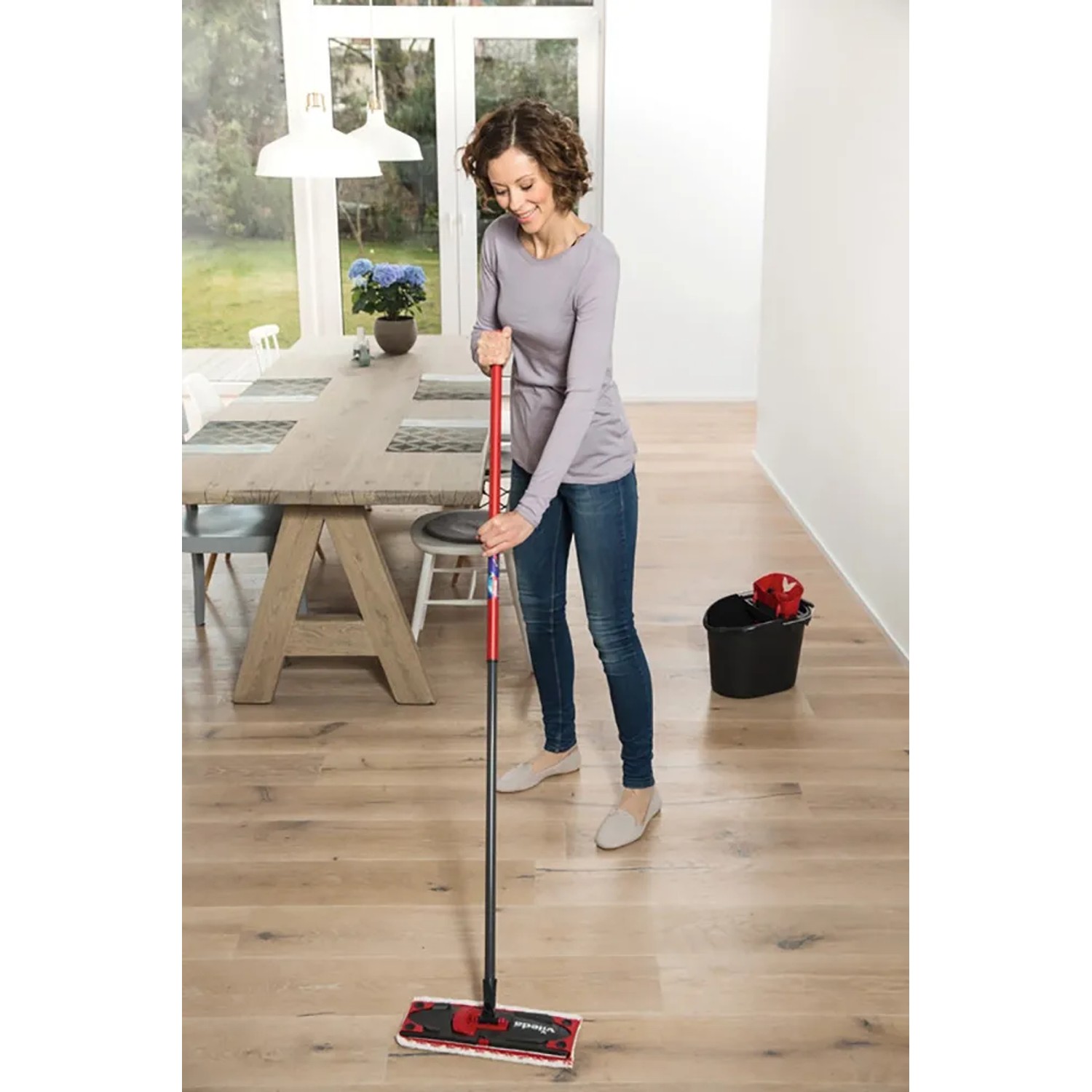 Frau wischt Holzboden mit Vileda Ultramax Reinigungssystem, Eimer im Hintergrund.