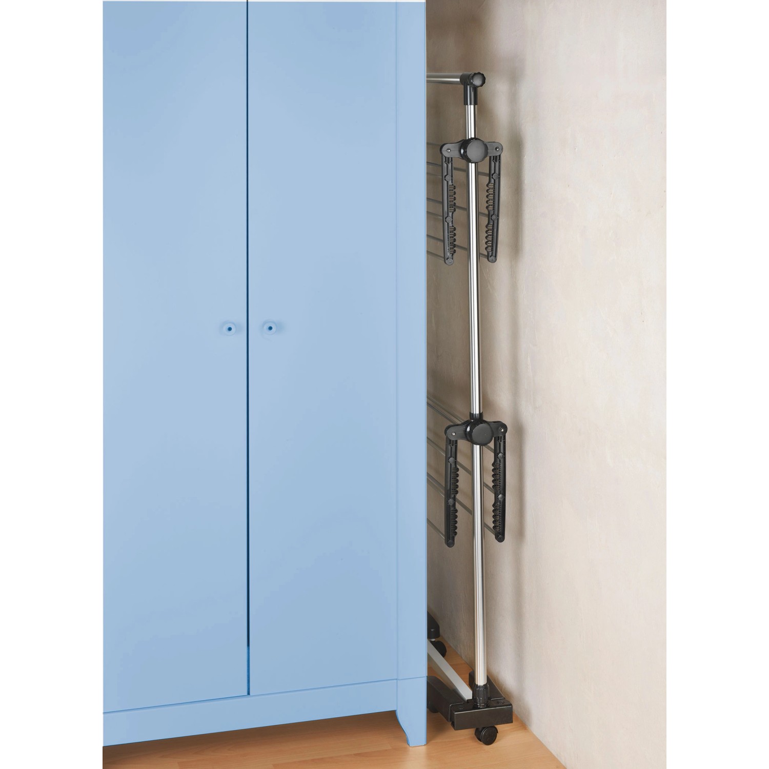 Zusammengeklappter, silberner Wenko Platzspar-Wäschetrockner neben einem blauen Schrank.