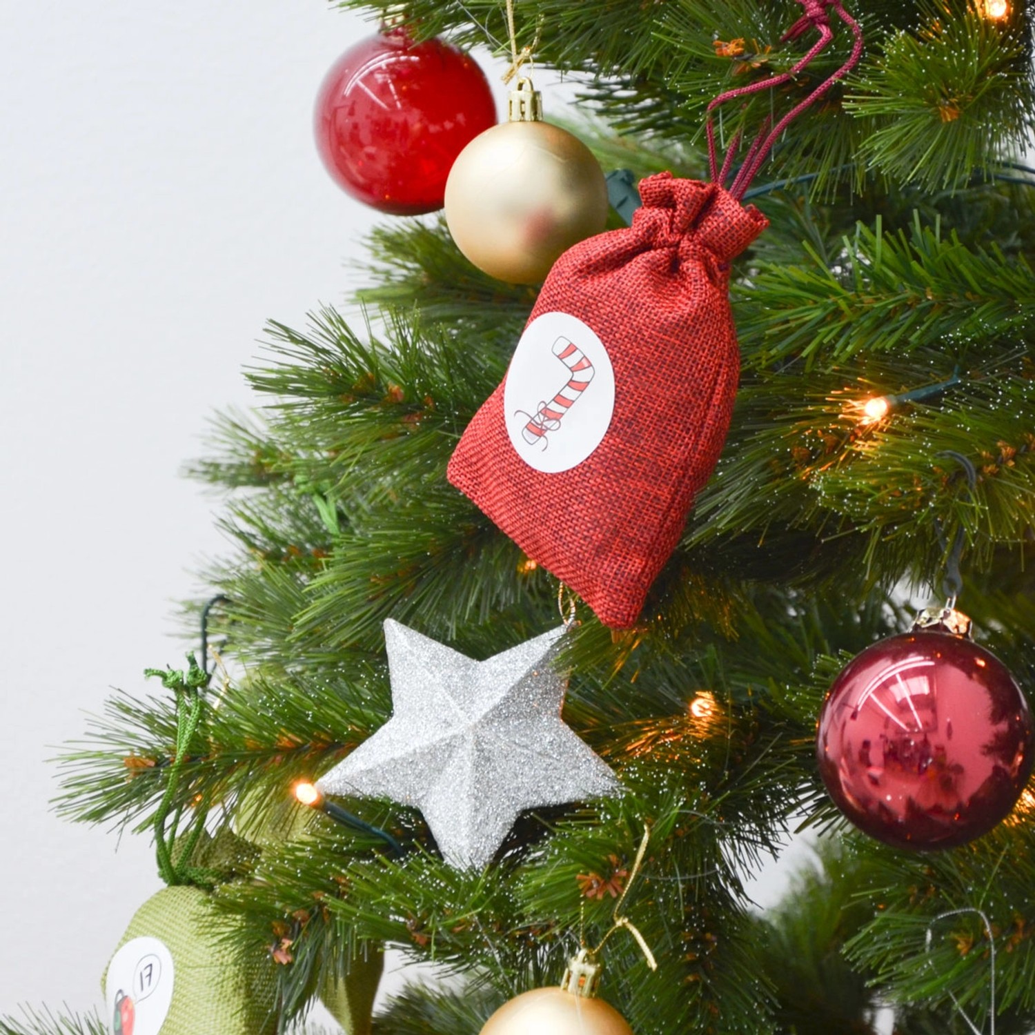 DIY Adventskalender Säckchen rot am Weihnachtsbaum mit Deko wie Kugeln und Stern.