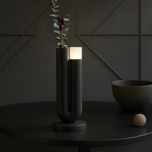 Moderne schwarze LED Tischleuchte Sayu mit integrierter Vase und Pflanzen auf dunklem Tisch. Dimmbar, kabellos.