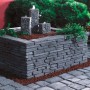 Ziermauer Madoc Schiefergrau mit Wasserfall und Bepflanzung im Garten.