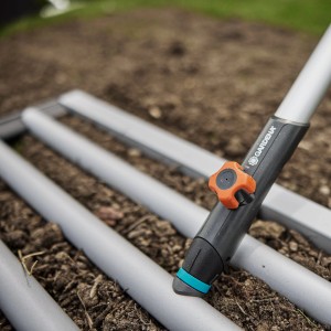 Gardena Combisystem-Rasenrakel (76 cm) im Einsatz auf Erde, Detailaufnahme.