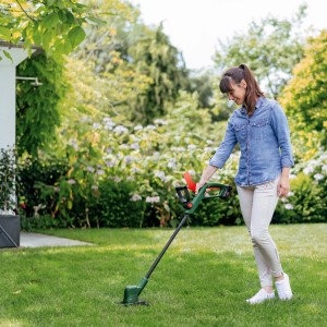 Frau trimmt Rasen mit dem Bosch Akku-Rasentrimmer EasyGrassCut 18V-26 Solo im Garten.