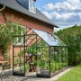 Schwarzes Halls Gewächshaus Qube 610 mit Pflanzen und Sitzgruppe im Garten.