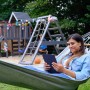 Frau entspannt in Hängematte vor Wickey Spielturm RocketFlyer mit Rutsche im Garten.