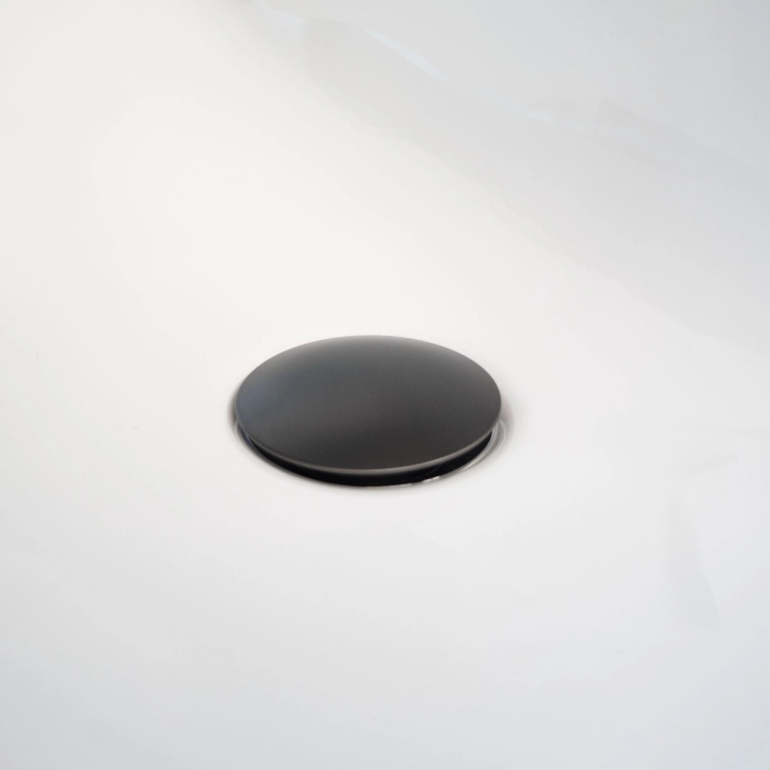 Detailaufnahme: Schwarzes Ablaufventil der Schöner Wohnen Kadia Waschtischarmatur auf weißem Waschbecken.